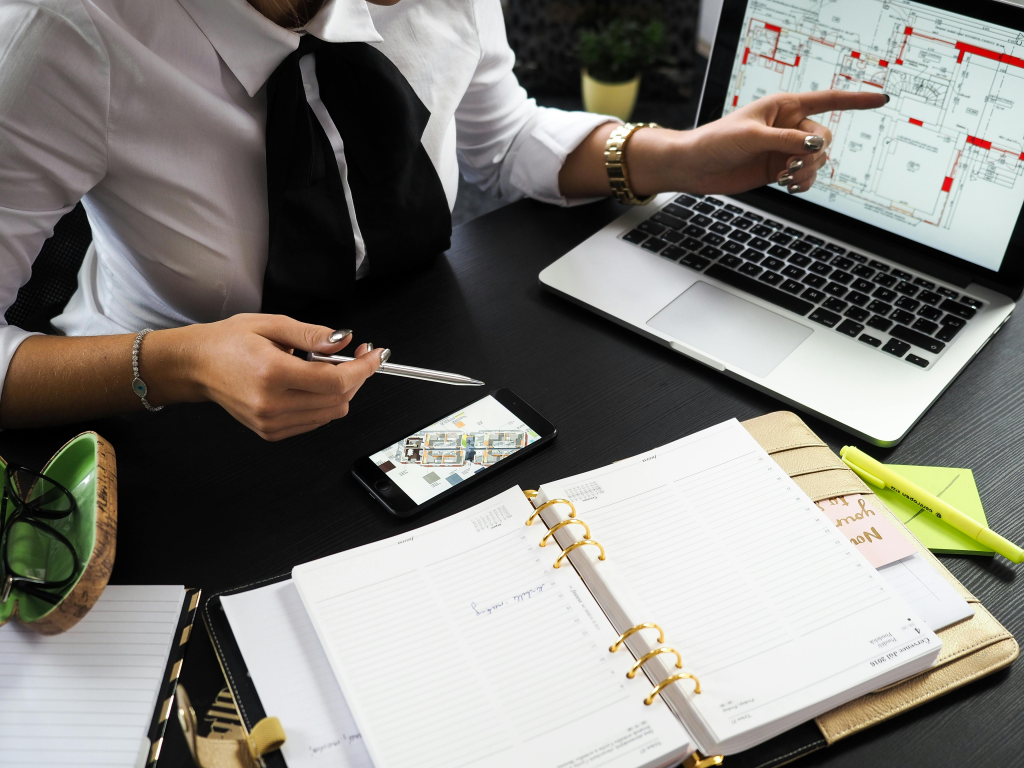 Professionnelle préparant l'organisation d'un événement à l'aide d'un ordinateur affichant un plan, d'un smartphone et d'un agenda.