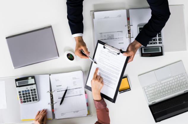 Deux professionnels échangent un contrat et un stylo sur un bureau pour formaliser un accord commercial.