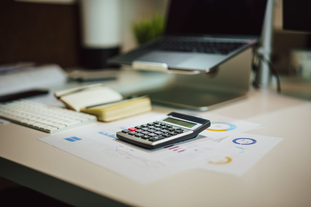 Calculatrice et documents posés sur un bureau à côté d'un ordinateur portable.